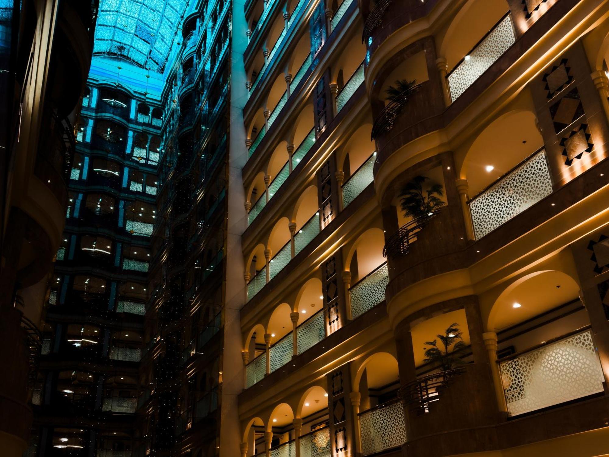Madinah Hilton Hotel Medina Exterior photo The photo shows the interior of a modern building, likely a hotel or a high-rise. The space features multiple floors with balconies that overlook a central atrium. The atrium is illuminated with warm lighting, enhancing the architectural details of t