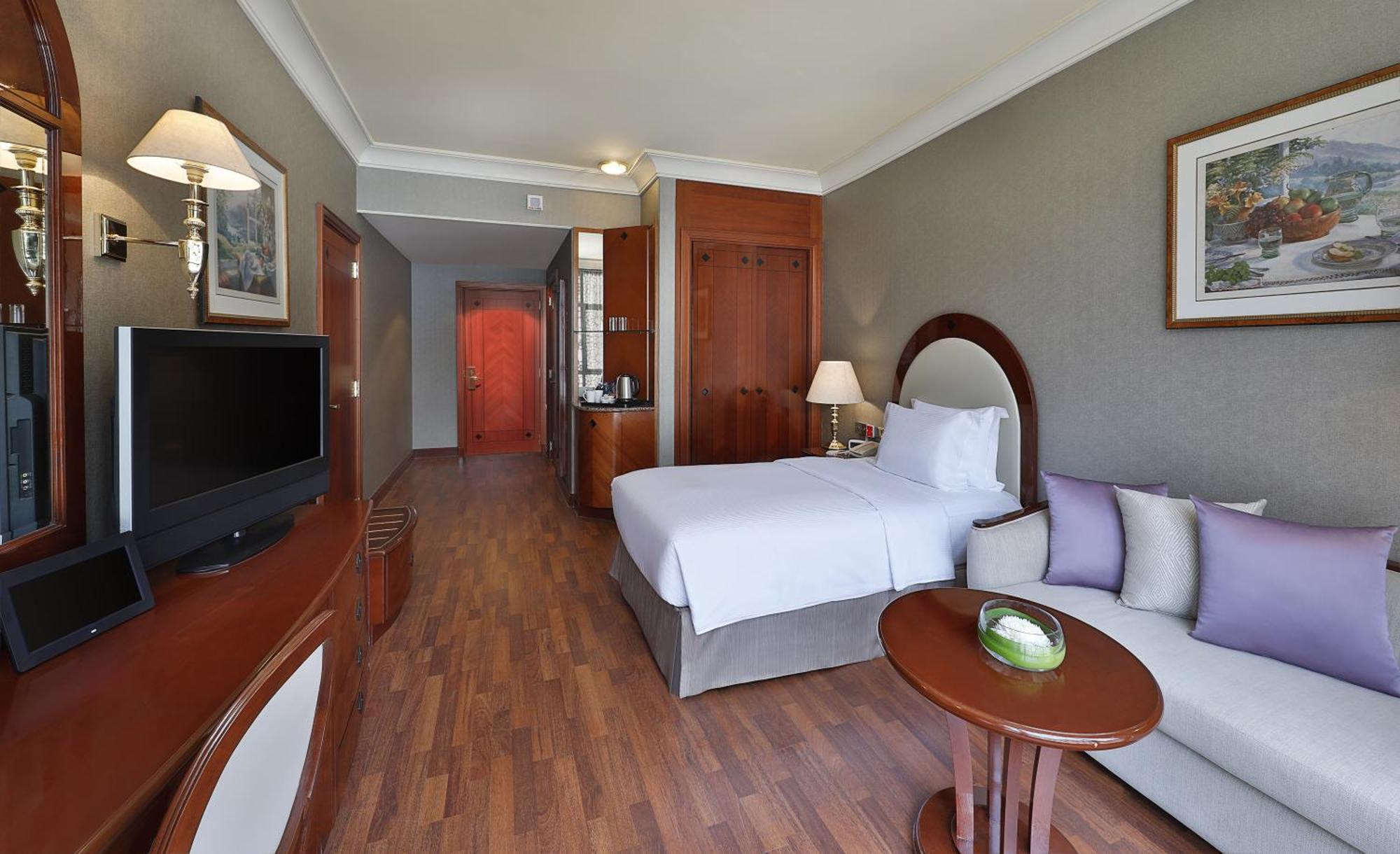 Madinah Hilton Hotel Medina Exterior photo The photo depicts a hotel room featuring a modern and tidy design. The room includes a single bed made with white linens, a small side table, and a comfortable sofa adorned with purple accent pillows. There’s a flat-screen television mounted on the w