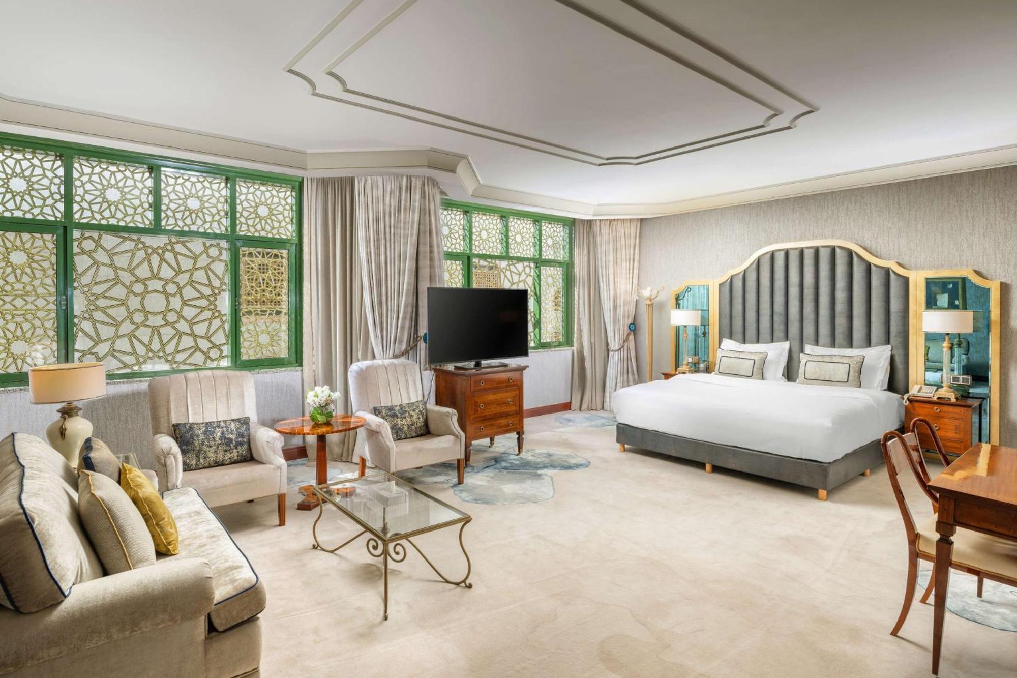 Madinah Hilton Hotel Medina Exterior photo The photo shows an elegantly designed hotel room. It features a large bed with a stylish headboard, complemented by decorative pillows. There are large windows with green accents that allow natural light to brighten the space. To one side, there's a 