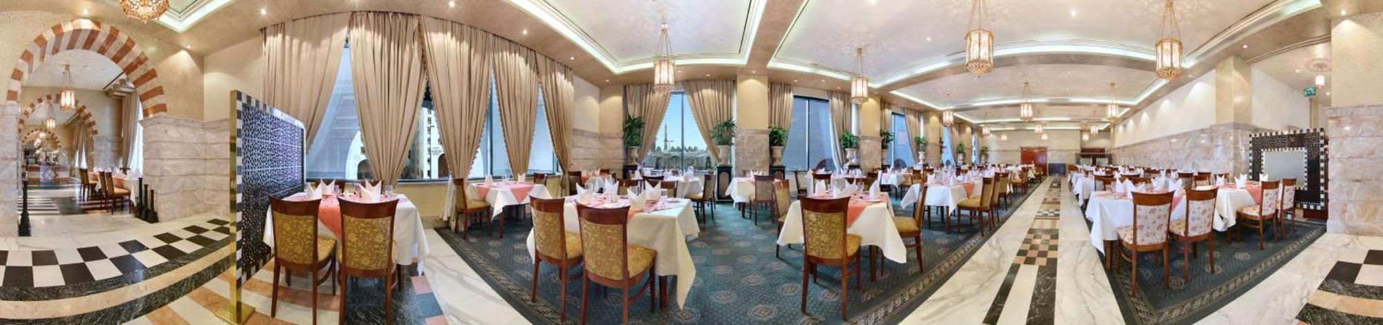 Madinah Hilton Hotel Medina Exterior photo The photo depicts an elegant restaurant interior. It features several dining tables, each set with white tablecloths and neatly arranged cutlery and napkins. The decor includes lavish curtains and potted plants, contributing to a warm and inviting at