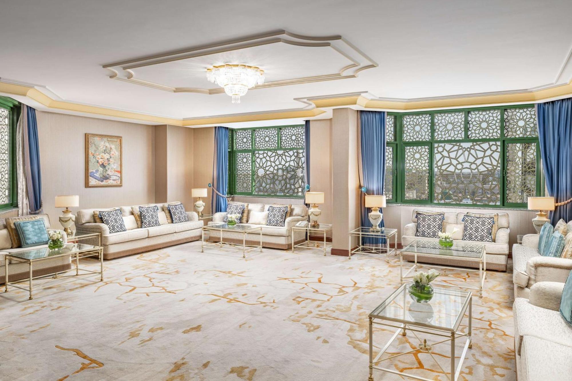 Madinah Hilton Hotel Medina Exterior photo The photo showcases a luxurious living room. The space features a light-colored carpet with a subtle pattern. It includes elegant seating arrangements with white sofas adorned with decorative cushions. There are large windows framed with blue curtain