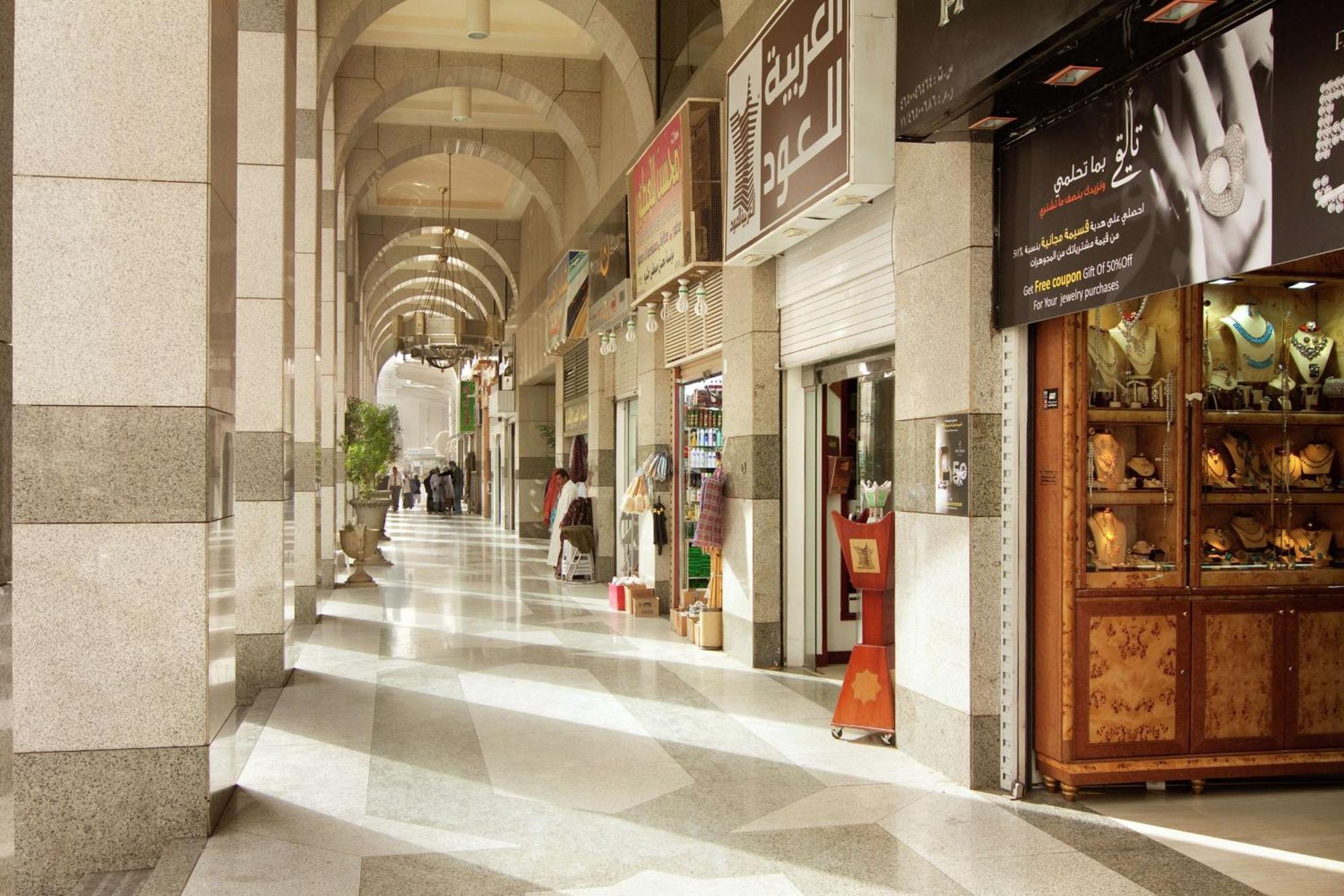 Madinah Hilton Hotel Medina Exterior photo The photo depicts an indoor marketplace or shopping arcade characterized by arched ceilings and a polished stone floor. On either side of the corridor, there are various shops with signage in Arabic. The shops appear to offer a range of goods, some o