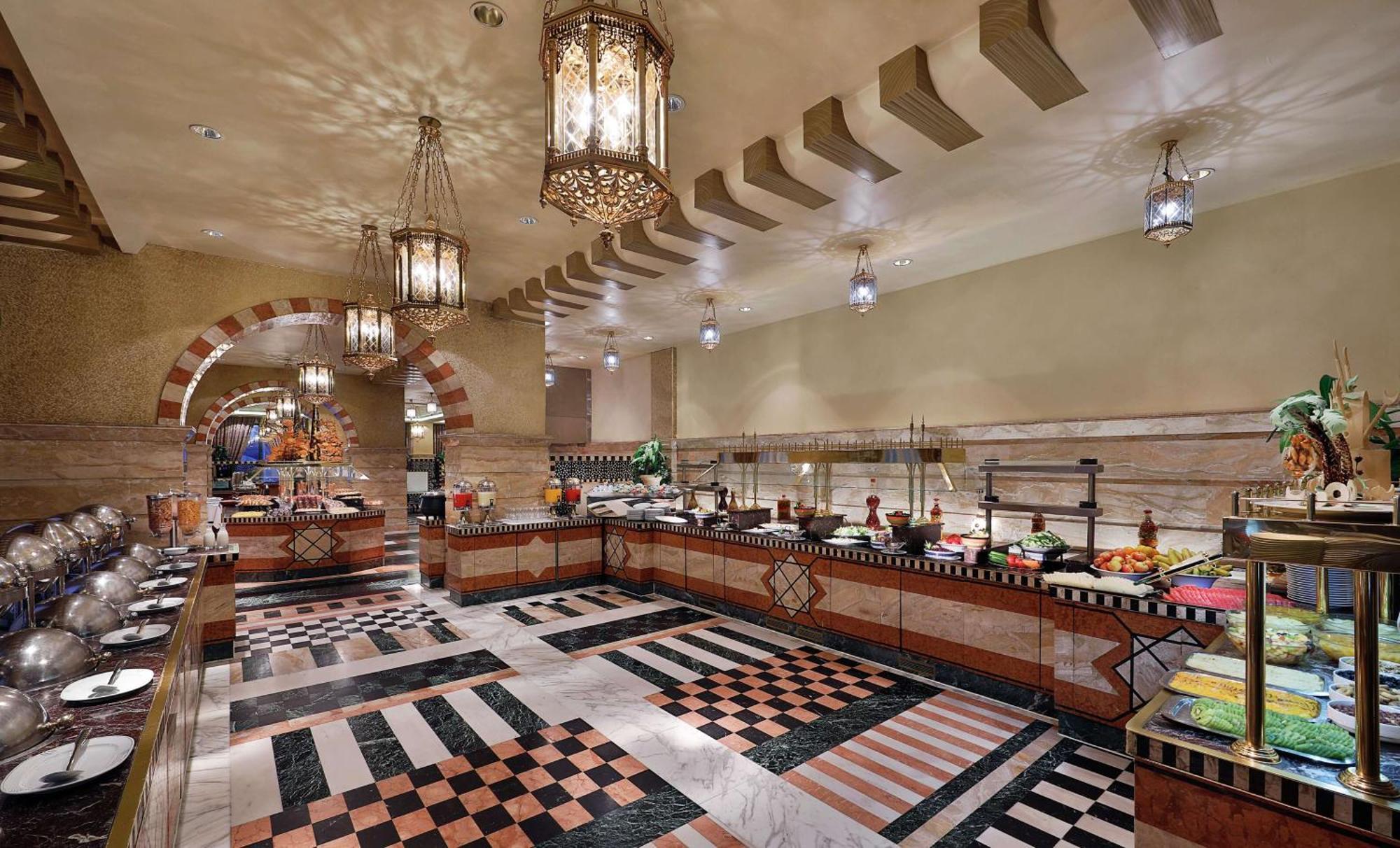 Madinah Hilton Hotel Medina Exterior photo The photo shows a spacious buffet area with a well-decorated interior. The room features intricate lanterns hanging from the ceiling, adding a warm ambiance. The flooring displays a bold black and white checkerboard pattern mixed with colorful tiles.