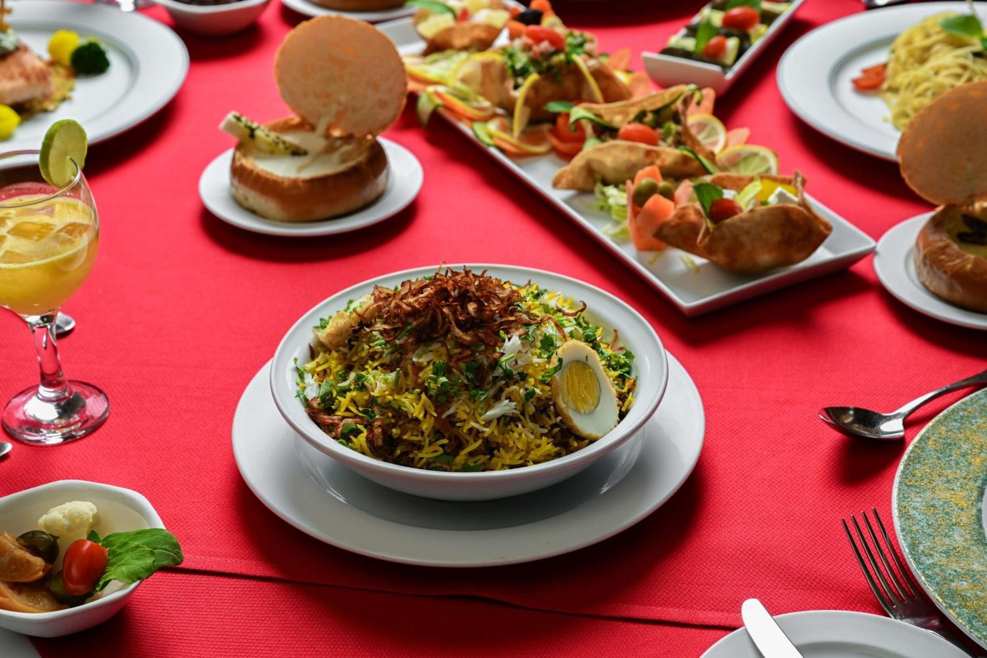 Madinah Hilton Hotel Medina Exterior photo The photo showcases a vibrant dining spread on a red tablecloth. In the center, there is a bowl of biryani, a flavorful rice dish that includes mixed vegetables and slices of boiled egg, topped with crispy fried onions. Surrounding the biryani are va