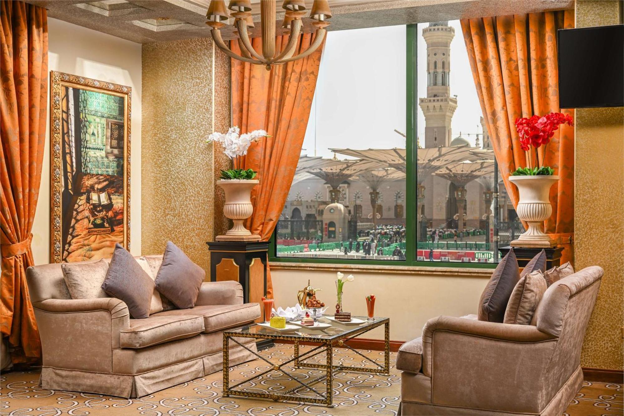 Madinah Hilton Hotel Medina Exterior photo The photo shows a stylish and elegantly furnished living area. It features two plush sofas with decorative cushions arranged around a glass coffee table, which holds refreshments and decorative items. Large windows dressed with orange curtains offer 