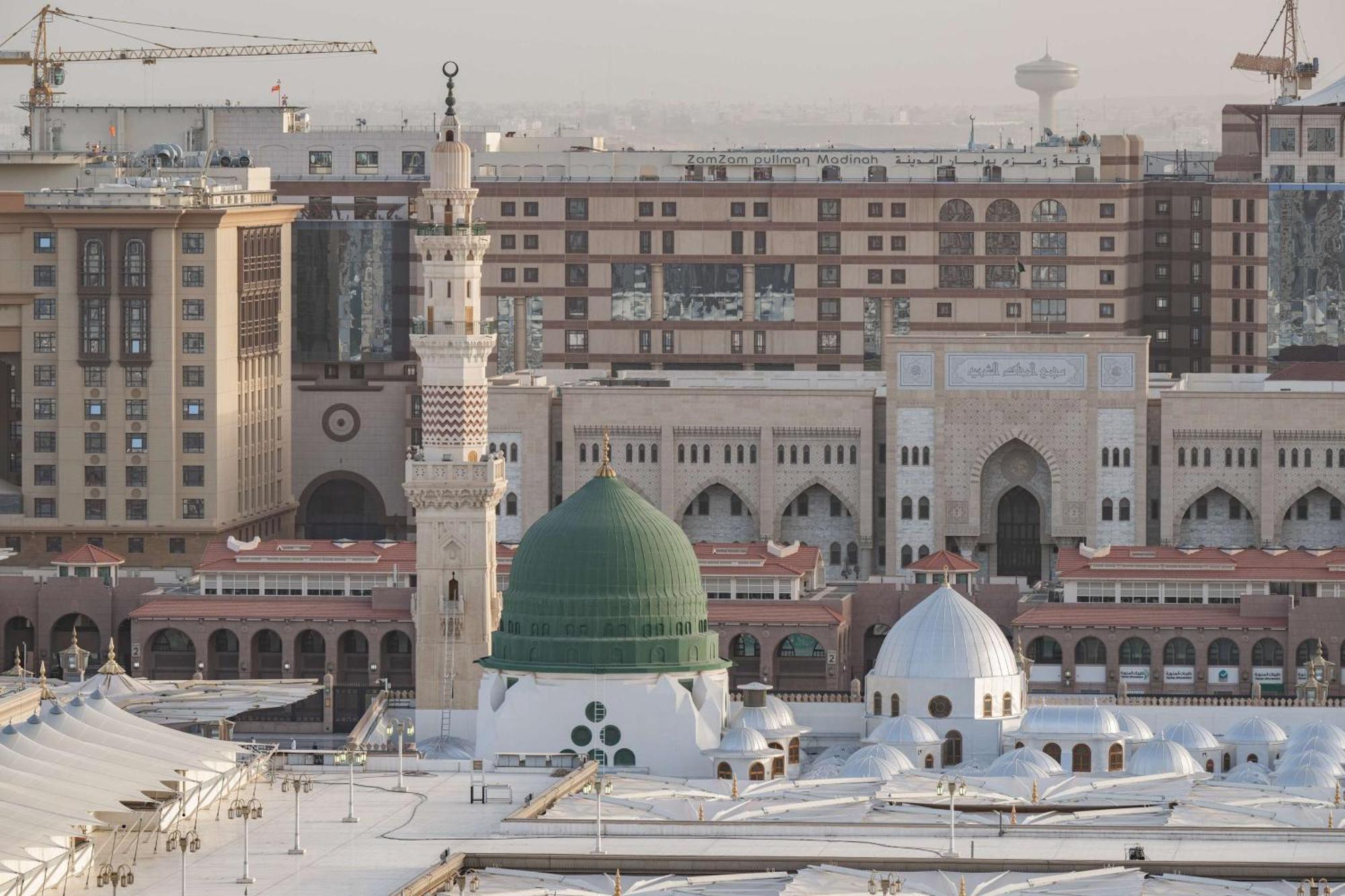 Madinah Hilton Hotel Medina Exterior photo The photo shows an aerial view of a prominent mosque complex, featuring a distinctive green dome and a tall minaret. The mosque is surrounded by modern buildings, indicating a blend of traditional Islamic architecture and contemporary structures. The