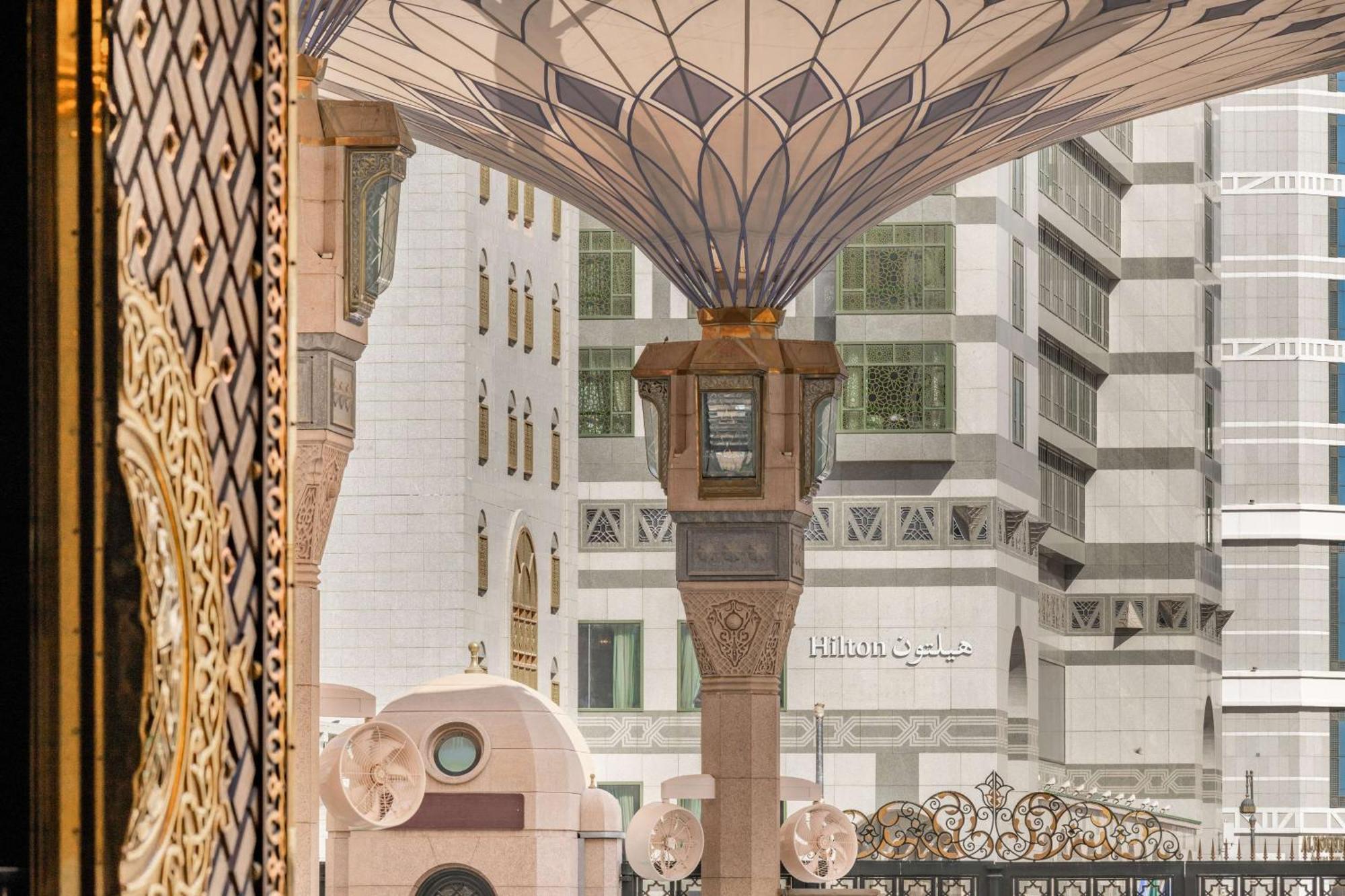 Madinah Hilton Hotel Medina Exterior photo The image shows a view of a large area with ornate architecture, featuring a prominent canopy with intricate design patterns. The structure appears to be part of a religious or public space, possibly a mosque, indicated by the decorative elements and