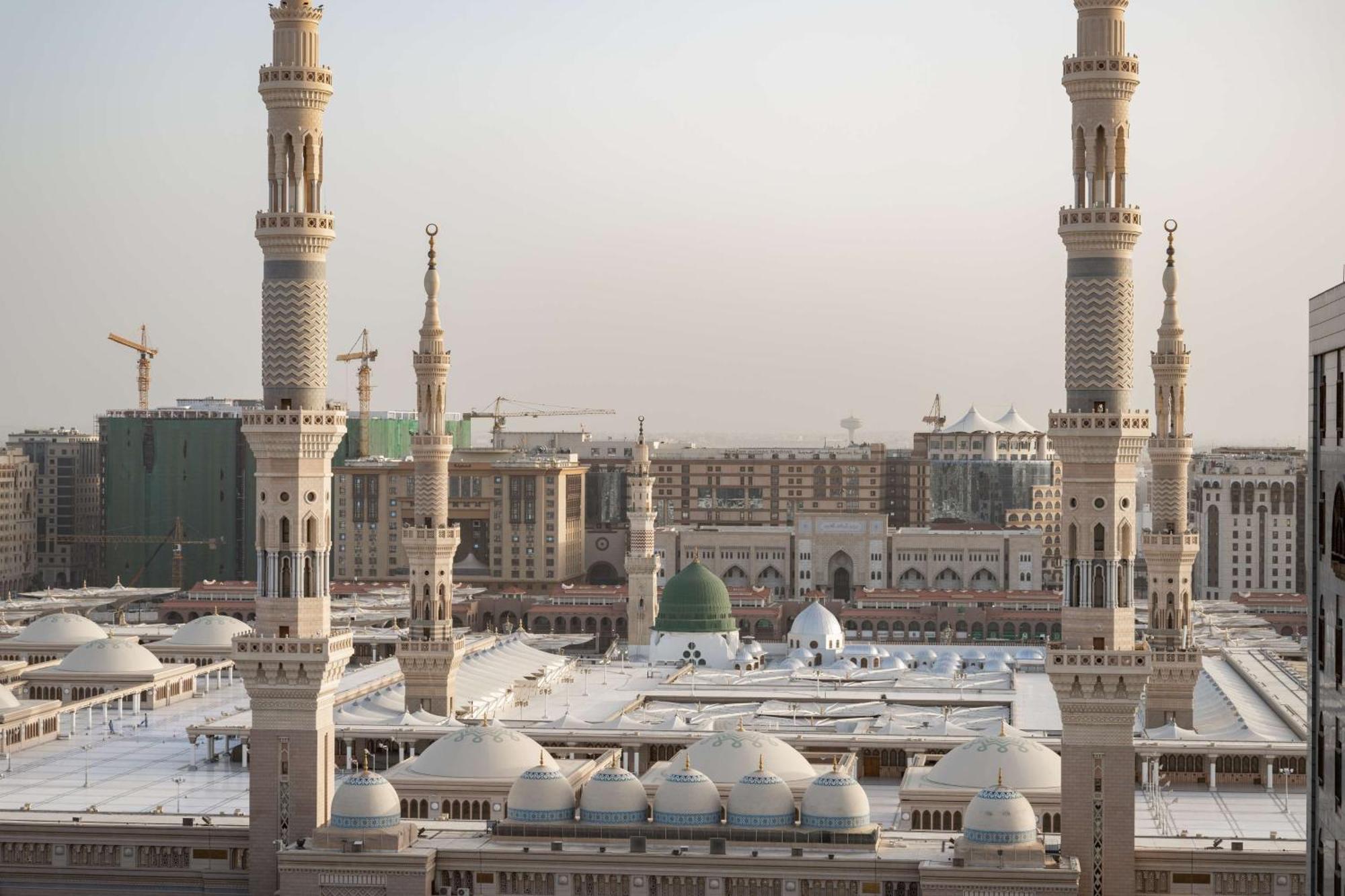 Madinah Hilton Hotel Medina Exterior photo The photo depicts a view of a mosque complex, prominently featuring multiple tall minarets and domes. The structures appear to be part of a large, intricately designed mosque that likely serves as a significant religious site. In the background, cons